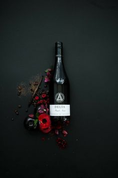 a bottle of delta next to some flowers on a black surface with red and pink petals