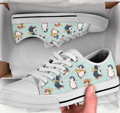 someone is holding their shoes up to show the penguin print on them, and it's in a box