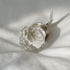 a clear glass object sitting on top of a white cloth covered table next to a metal hook