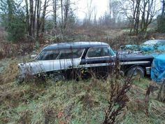 an old car is sitting in the middle of some tall grass and trees with blue tarps on it