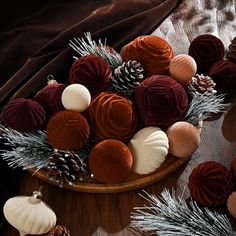 a wooden bowl filled with different types of christmas decorations and pine cones on top of a table