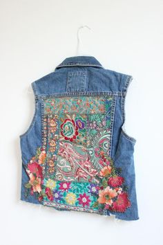 the back of a jean jacket with embroidered flowers and paisley designs on it, hanging from a white wall