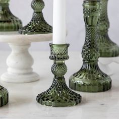 green glass candlesticks sitting next to each other on a white marble countertop