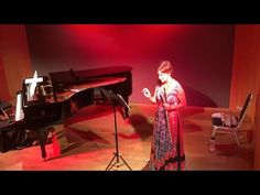 a woman is standing in front of a piano and singing into a microphone on stage