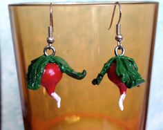 a pair of red and green earrings sitting on top of a glass cup next to a vase