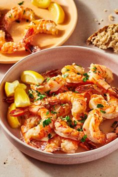 a bowl filled with shrimp next to bread and lemon wedges