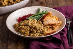 a white plate topped with meat and veggies next to a bowl of stuffing