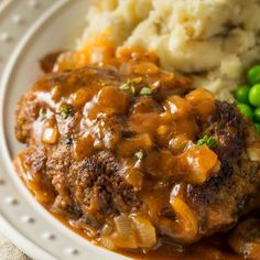 a white plate topped with meat covered in gravy next to mashed potatoes and peas