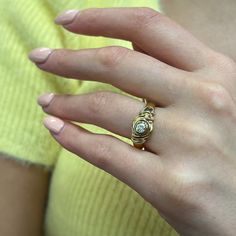 a woman's hand wearing a gold ring with a white diamond in the middle