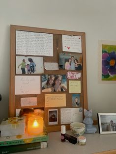 a wooden frame with pictures and photos on it next to a lit candle in front of some books