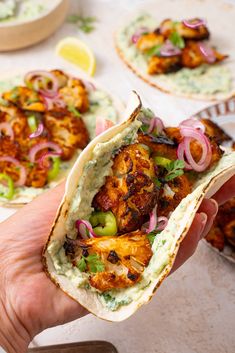 a hand holding a taco filled with chicken, onions and cilantro sauce