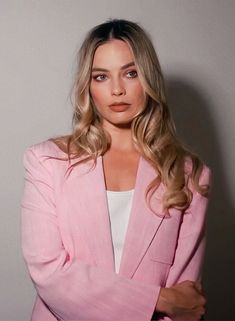 a woman in a pink blazer and white top is posing for the camera with her arms crossed