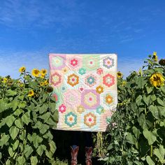 a person standing in front of a field of sunflowers holding up a quilt