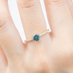 One of a kind ring In stock ready to ship in size 7 0.75ct 5.5mm teal blue Montana sapphire 0.03ctw G color SI clarity accent diamonds Band width: approx. 1.4mm Low profile four prongs basket setting Made of 100% recycled solid 14k yellow gold and ethically sourced gemstones Packaged in a white craft paper ring box Blue Diamond Birthstone Ring For Promise, Blue Diamond Birthstone Promise Ring, Moissanite Sapphire Ring For Proposal, Gift Sapphire Diamond Ring, Sapphire Diamond Ring As A Gift, Blue Diamond Birthstone Ring With Accent Stones, Blue Round Cut Diamond Ring, Blue Diamond Ring With Round Cut, Blue Cubic Zirconia Diamond Ring With Prong Setting