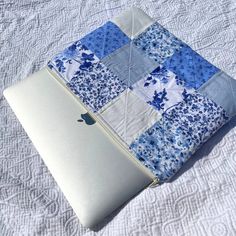 an apple laptop computer sitting on top of a quilted bed cover with blue and white flowers