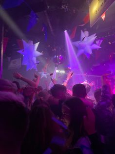 a crowd of people at a party with purple and blue lights on the ceiling, stars hanging from the ceiling