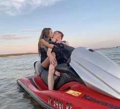 two people riding on the back of a red and black jet ski in the water