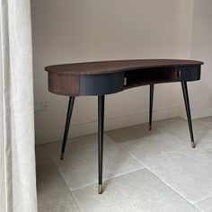 a wooden desk with two black legs and a white wall in the corner behind it