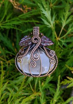 a wire wrapped glass ornament hanging from a tree with green leaves in the background