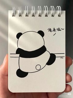 a hand holding a spiral notebook with an image of a panda on it