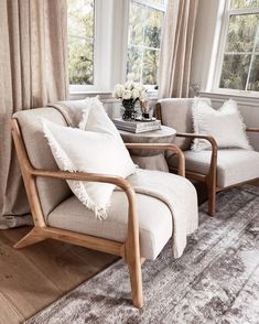 a living room with two chairs and a table in front of a window that has curtains on the windowsill