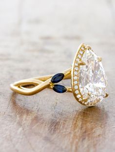 a diamond and blue sapphire ring on top of a wooden table with gold plating