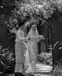 black and white photograph of two people in front of an arch with flowers on it