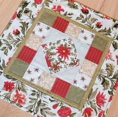 a quilted table topper with red and white flowers on it, sitting on a wooden floor