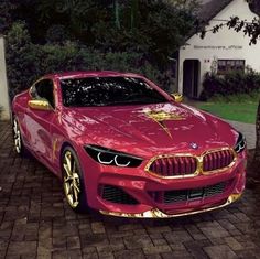 a red car with gold trim parked in front of a white house and trees on the sidewalk