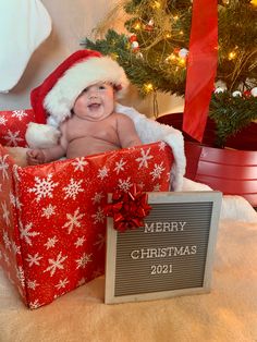 a baby wearing a santa hat sitting in a gift box with a merry christmas sign next to it