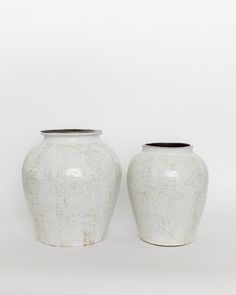 two white vases sitting next to each other on a white surface with no one in it