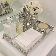 a silver tray topped with white flowers next to a bathroom mirror and sink filled with personal care items