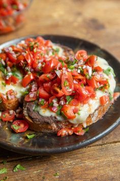 an open face sandwich topped with tomatoes and green onions on a black plate sitting on a wooden table