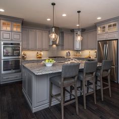 a large kitchen with gray cabinets and marble counter tops, stainless steel appliances and wooden flooring