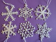 four snowflakes are hanging from strings on a purple surface, one is white and the other is black