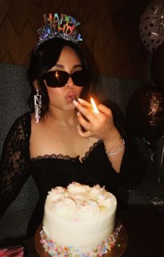 a woman blowing out the candles on her birthday cake while wearing sunglasses and a tiara