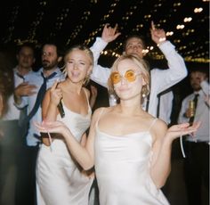 two women in white dresses standing next to each other on a dance floor with their arms raised