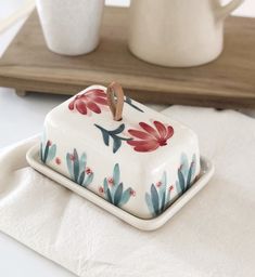 a white and red flowered ceramic dish on a tray with two cups in the background