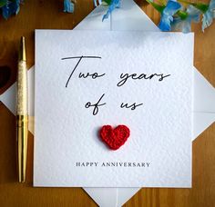 two years of us anniversary card with a red heart on it next to a pen and flowers