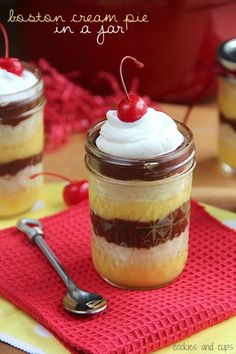 two desserts with whipped cream and cherries in a jar on a red napkin