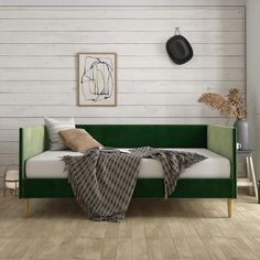 a green couch sitting on top of a hard wood floor next to a white wall