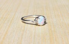 This stunning white lab opal has amazing flashes of color, it compliments a large variety of accent colors. The white opal is hand set, along with cubic zirconia accent stones, into an elegant sterling silver setting. Select your choice of side accent stones to create a unique custom ring...Setting Material - Stamped 925 Sterling SilverCenter Gemstone-Gemstone: OpalType: Lab CreatedColor: WhiteSize: 8 x 6mm Shape: Oval  Accent Gemstones-Gemstone: Cubic ZirconiaType: Lab CreatedColor: Your choice White Topaz Engagement Ring, Pink Opal Ring, Sterling Silver Opal Ring, Opal Diamond Ring, Ring Inspo, Silver Lab, Silver Opal Ring, White Opal Ring, Ethiopian Opal Ring