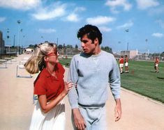 a man and woman walking on a baseball field with the sky in the back ground