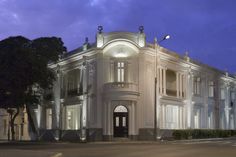 a large white building sitting on the corner of a street at night with its lights on