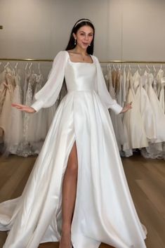 a woman in a white dress standing next to some wedding gowns and dresses on racks