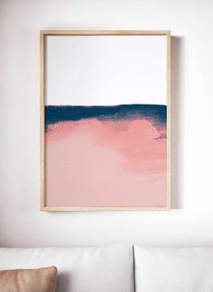 a pink and blue painting hangs on the wall above a white couch in a living room