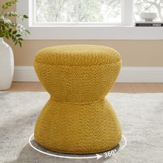 a yellow ottoman sitting on top of a rug in front of a white vase and window