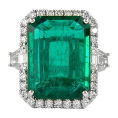 Stunning emerald of superb color and diamond three stone ring with halo, GIA certified. High jewelry by Alexander Beverly Hills. 14.58 carats total gemstone weight. *Center emerald faces up like a 20ct stone 13.18 carat emerald cut emerald, GIA certified F2. 2 trapezoid cut diamonds, 0.79 carats, approximately I/J color, VS clarity. Complimented by 26 round brilliant diamonds, 0.61 carats. Approximately G/H color and VS clarity. 18k white gold, 8.27 grams, current ring size 6.75. Accommodated with an up-to-date appraisal by a GIA G.G. once purchased, upon request. Please contact us with any questions. Item Number R9503 Colombian Emerald Ring, Emerald And Diamond Ring, Spinel Ring, Platinum Diamond Rings, Cushion Cut Ring, Emerald Diamond Ring, Cushion Ring, Colombian Emeralds, Diamond Cocktail Rings