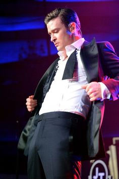 a man in a tuxedo standing on stage with his hands behind his back