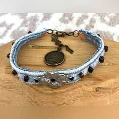 a blue bracelet with an antique medallion and black beads on the clasp is sitting on top of a wooden board